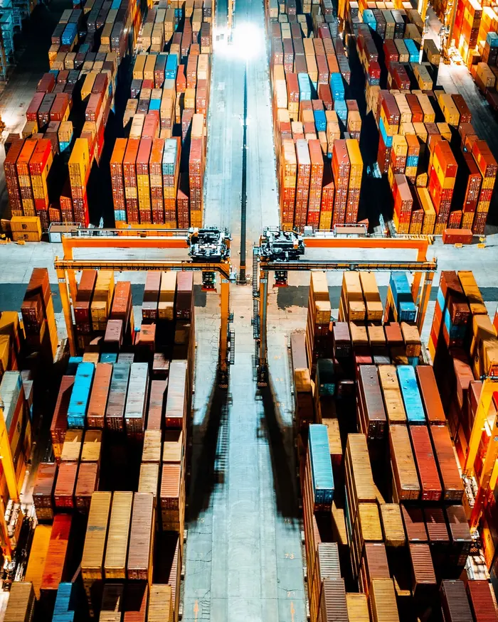 Aerial view of stacked shipping containers being handled by a gantry crane